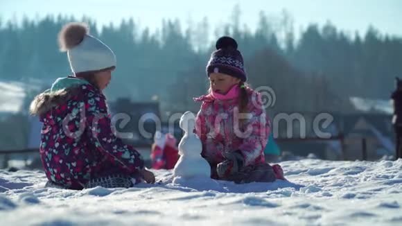 穿着户外运动的孩子在雪地里玩耍时堆起小雪人背景是群山视频的预览图