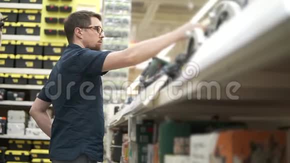 男性购物者正在一家建筑工具商店里拿着摆动的电动工具视频的预览图