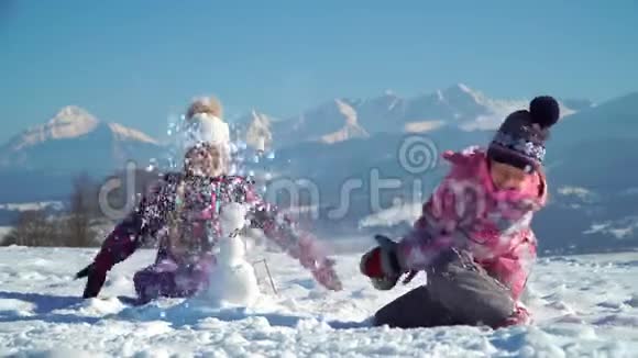 穿着户外运动的孩子在雪地里玩耍时堆起小雪人背景是群山视频的预览图