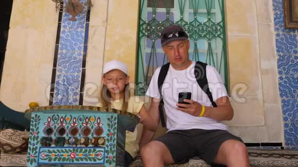 女儿和父亲用电话坐在房子附近有传统的阿拉伯图案视频的预览图