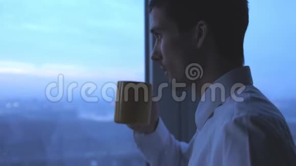 年轻的商人在办公室喝茶晚上从窗口欣赏风景3840x2160视频的预览图