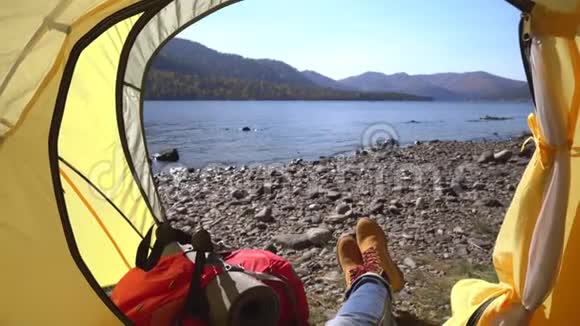 女旅行者躺在湖边的一个黄色帐篷里手里拿着智能手机然后是视频的预览图