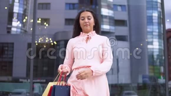 年轻的女孩穿着粉红色的裙子购物后手里拿着包裹心情很好慢动作高清高清视频的预览图