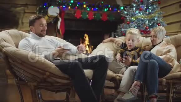 男人喝咖啡而女人和小男孩则在看智能手机上的视频在圣诞夜大笑视频的预览图