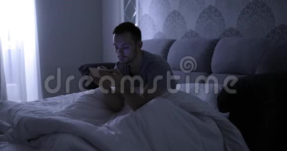 晚上睡觉前带着智能手机躺在床上的男人视频的预览图
