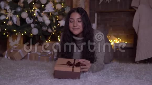 女孩拿着礼物打开盒子高兴地躺在圣诞树附近的地板上高清高清视频的预览图