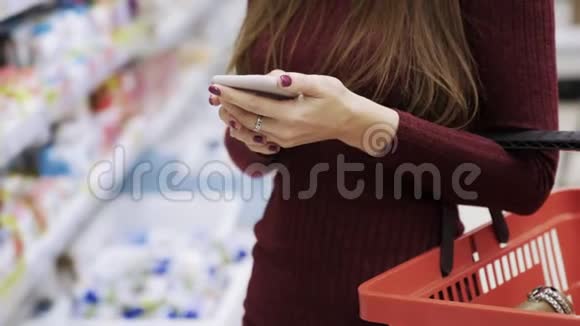在超市商店里用智能手机和食物篮把女人的手收起来视频的预览图