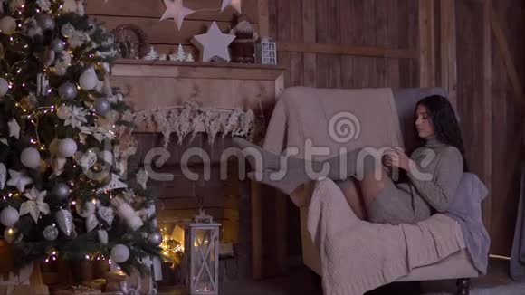 圣诞节一个女孩坐在圣诞树附近的椅子上喝茶高清高清视频的预览图
