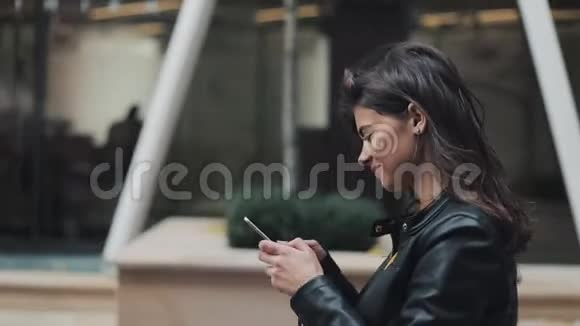 年轻快乐的女人在城市街道上散步同时使用智能手机她从电话里翻译了一个视图看了看视频的预览图