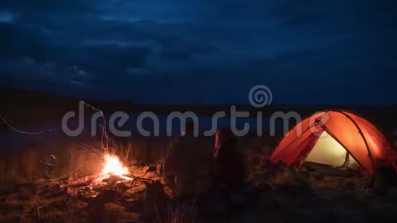 晚上露营时无法辨认的情侣的时间推移和池塘附近的火焰视频的预览图