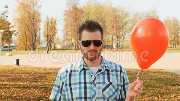 时髦的长胡子手里拿着太阳镜和一个红色气球视频的预览图