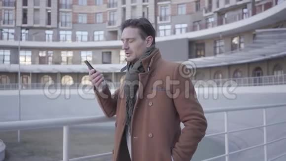 一幅漂亮的成功男人穿着棕色外套站在城市街道上用手机说话的肖像城市景观视频的预览图