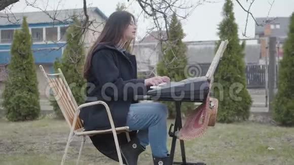 美丽的黑发女孩热衷于玩合成器坐在后院的树下唱歌视频的预览图