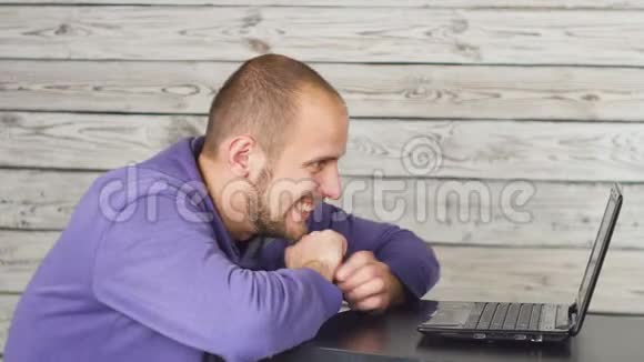 微笑的男人坐在办公室用笔记本电脑工作亲吻显示器成功视频的预览图