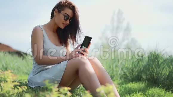 年轻的女人坐在草地上和朋友在公园里聊天视频的预览图
