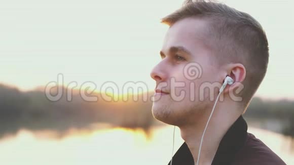 年轻的帅哥在日落时在海滩上听音乐慢动作透镜耀斑效应视频的预览图