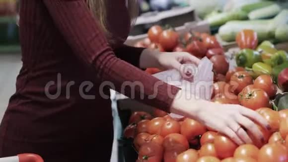 女人用新鲜蔬菜从柜台把番茄放进塑料袋里视频的预览图