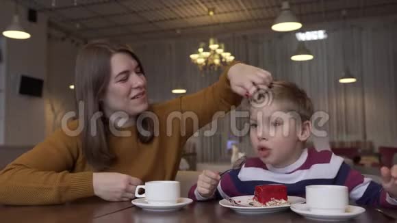 一位可爱的年轻母亲和一个小儿子在咖啡馆里吃着美味的甜点视频的预览图