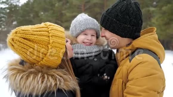 爸爸妈妈在冬天公园拥抱和亲吻他们的小儿子视频的预览图