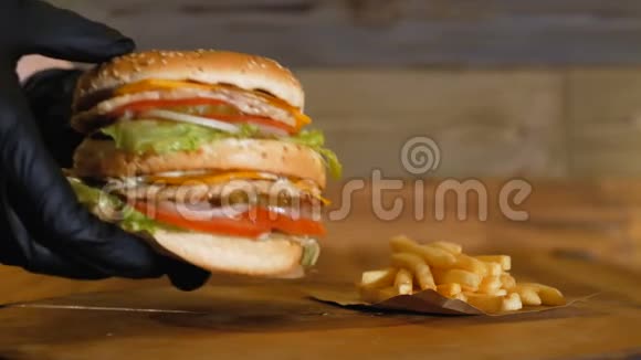 黑色手套在薯条旁边的木板上放了一个多汁的汉堡上面有两个小切和蔬菜不健康视频的预览图