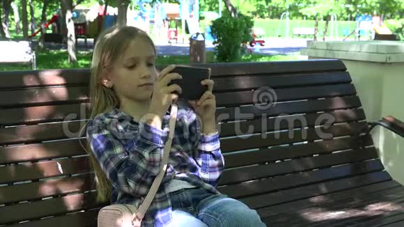 公园操场上玩平板电脑的孩子坐在长凳上的女孩4K智能手机视频的预览图