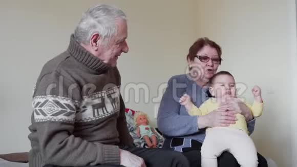 快乐的爷爷奶奶在家里和一个蹒跚学步的玩耍视频的预览图