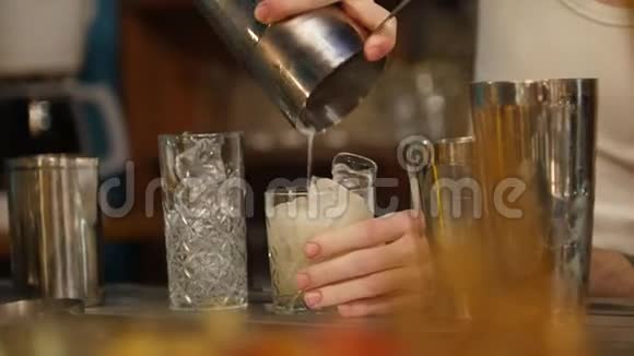 年轻的职业酒保把白色的奶油饮料倒入盛满冰块的杯子里然后在上面放一个泡菜视频的预览图