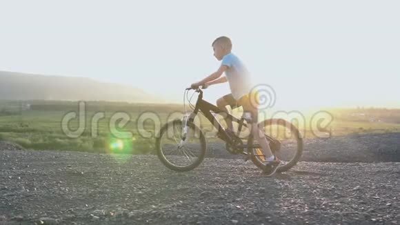 小男孩骑自行车在夏季山顶美丽的日落天空背景八岁的白种人小男孩视频的预览图