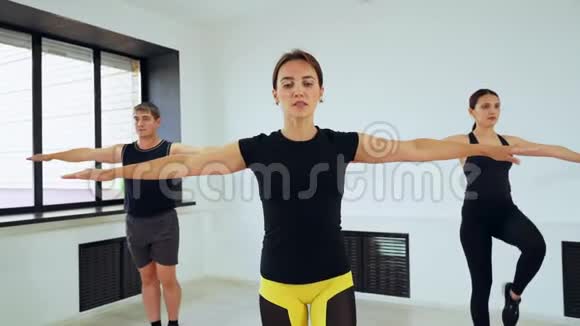 一个男人有两个女孩站在一条腿上手臂伸到两边一群人在做普拉提视频的预览图