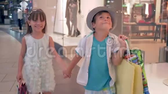 快乐购物时髦的小男孩和小女孩购买后手里拿着包裹在黑色的时候穿过商店橱窗视频的预览图