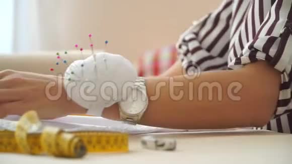 一个年轻女孩的手拿着钟光滑的白布裁缝用铅笔在织物上做笔记视频的预览图