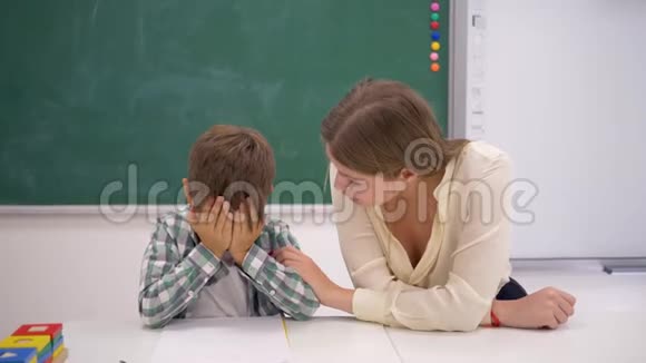 教育工作者在课外活动中在教室黑板旁的书桌旁安抚哭泣的学童视频的预览图