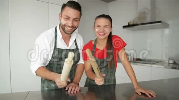 一对夫妇一起做一个有趣的面孔现代厨房里穿着围裙的白种人男子和女孩视频的预览图