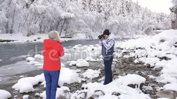 冬天的摄影师在雪的背景下在山河附近拍摄女孩视频的预览图