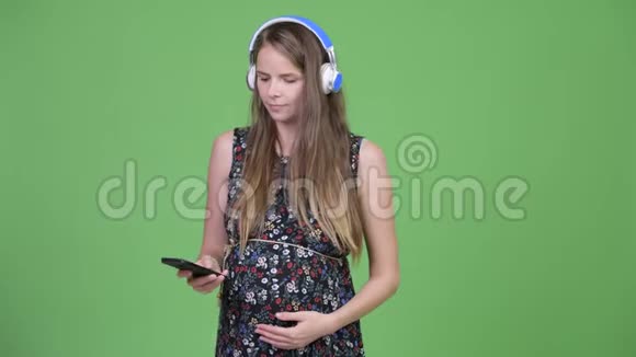 年轻快乐的孕妇一边听音乐一边用电话视频的预览图