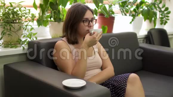 漂亮的女孩坐在沙发上在诊所等候轮到她时喝茶视频的预览图