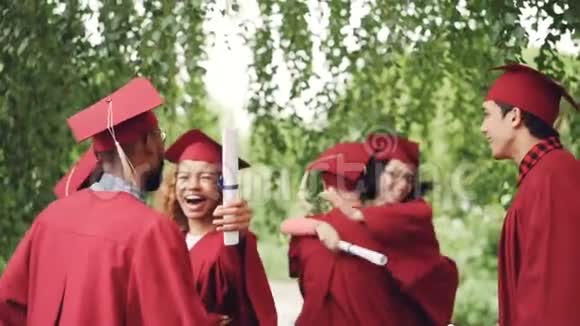 毕业典礼结束后快乐的毕业学生多民族的一群人拥抱着做着高五女孩和男孩都在视频的预览图