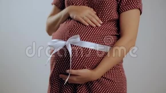 孕妇双手捧腹腹部有白色丝带健康理念白色背景视频的预览图