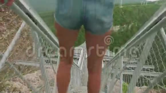 年轻的白种人金发女郎靠在山峡上方的吊桥栏杆上跳跃特写视图视频的预览图