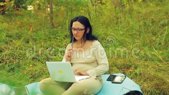 一个在森林边缘戴眼镜的体贴的女人手里拿着一支铅笔和一台笔记本电脑找到了解决办法视频的预览图