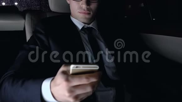 年轻的商人坐在汽车后座上使用智能手机夜景视频的预览图