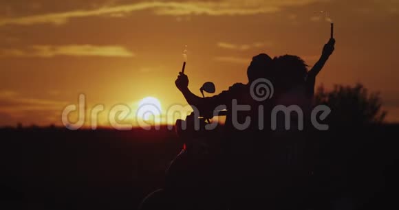 日落时分年轻夫妇在黑色复古摩托车后面玩得很开心手里拿着火花享受着快乐视频的预览图