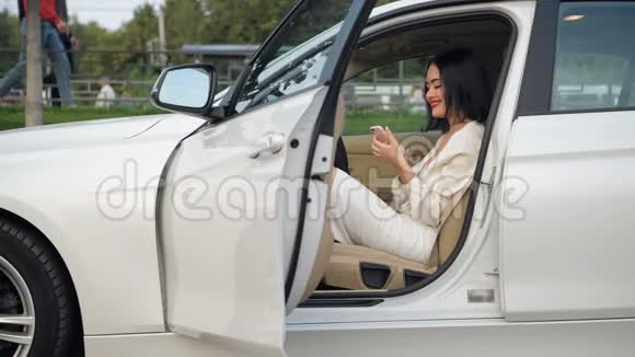 优雅的商务女性在停车场的一辆白色汽车里通过智能手机打电话视频的预览图