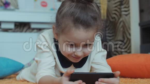 漂亮的小女孩在玩电话躺在针织地毯上玩平板电脑视频的预览图