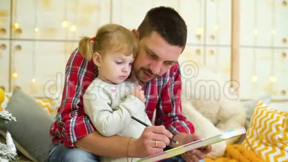 年轻的父亲教蹒跚学步的女儿画画视频的预览图