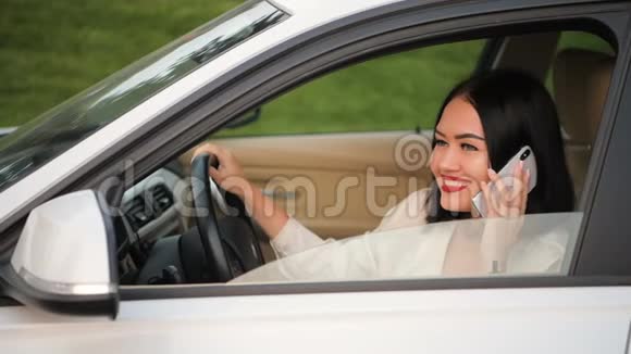 优雅的黑发商务女性坐在汽车的方向盘上打电话视频的预览图