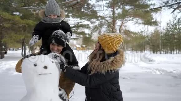 年轻的家庭妈妈儿子和爸爸正在冬季城市公园堆雪人视频的预览图