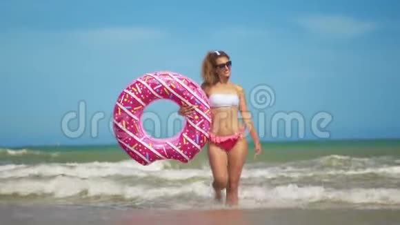 年轻女子在海滩上玩玩具充气戒指甜甜圈视频的预览图