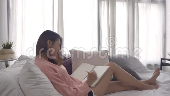 慢动作年轻的亚洲女人在假期看书年轻快乐的女孩坐在家里的沙发上打开了书视频的预览图