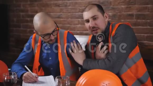 两名工人戴着安全帽休息喝着咖啡在建筑办公室休息视频的预览图